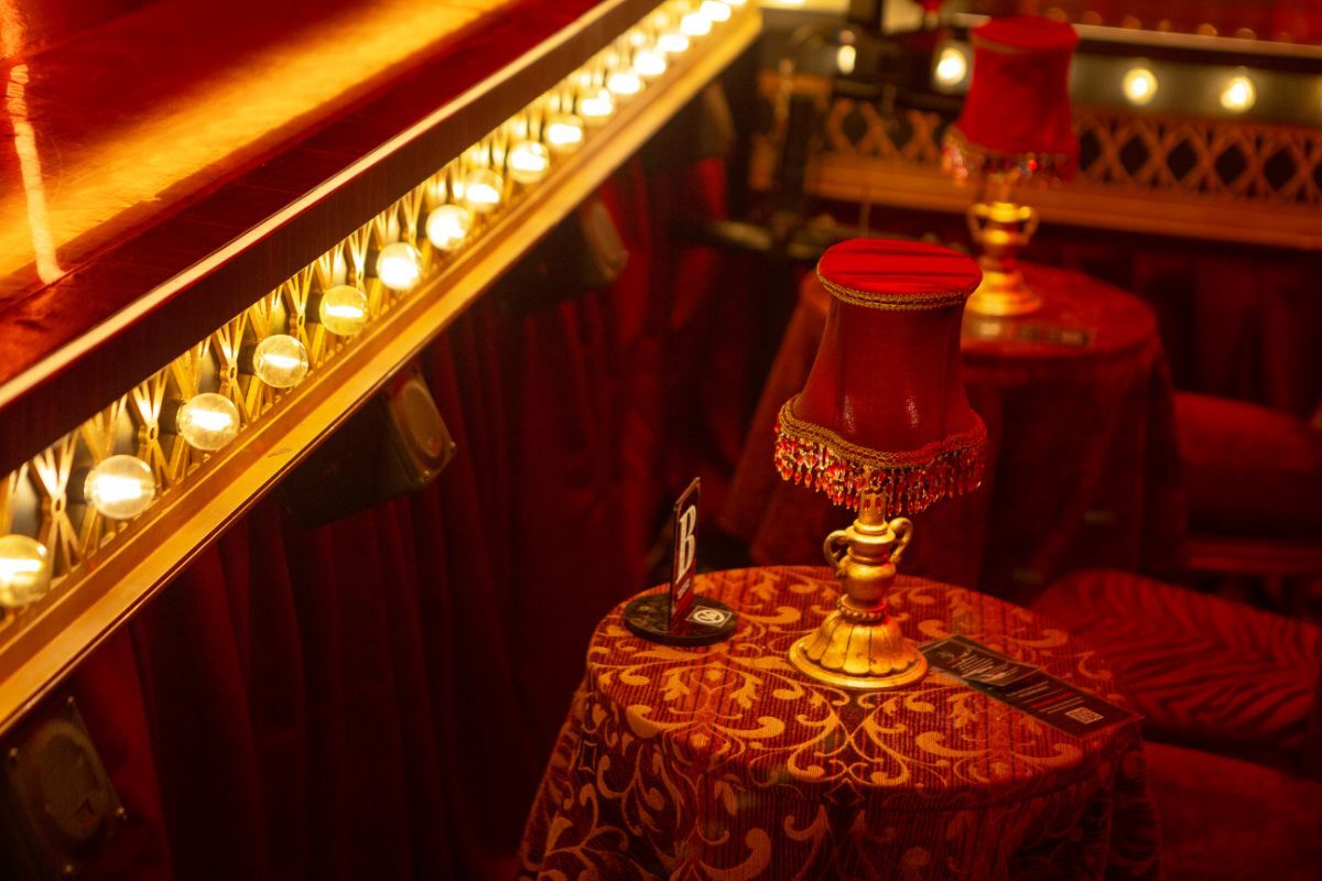 A small cabaret-style table covered in patterned red fabric and topped with a gold lamp, part of Reveal Productions’ upholstery work for Moulin Rouge.