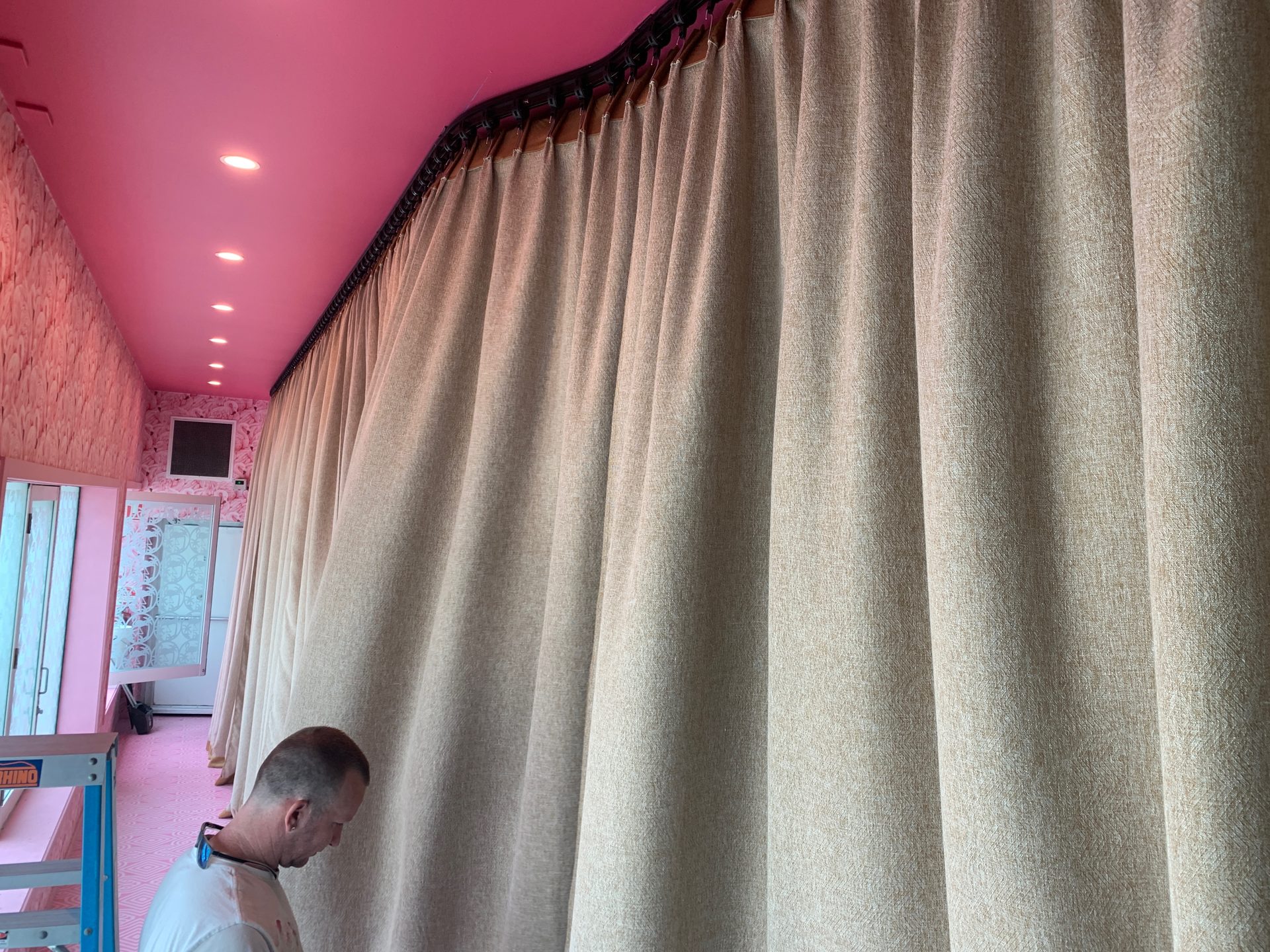Installer working beneath a newly hung pleated drape on ceiling track