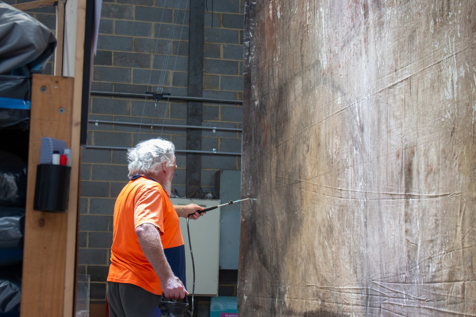 Reveal technician spray-cleaning a painted scenic backdrop cloth hung at the workshop